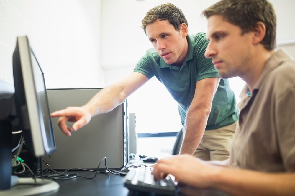 Side view of teacher showing something on screen to mature student in the computer room